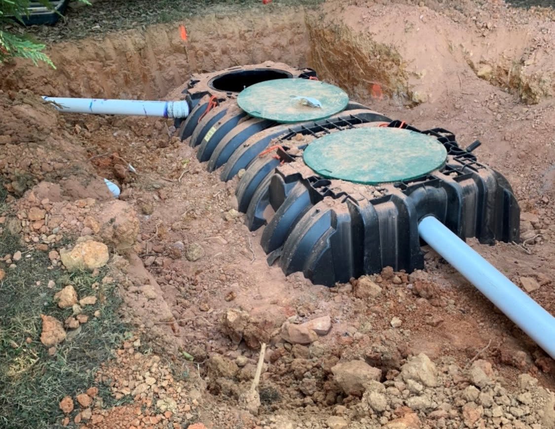 A plastic septic tank in an excavated hole with inlet and outlet pipes